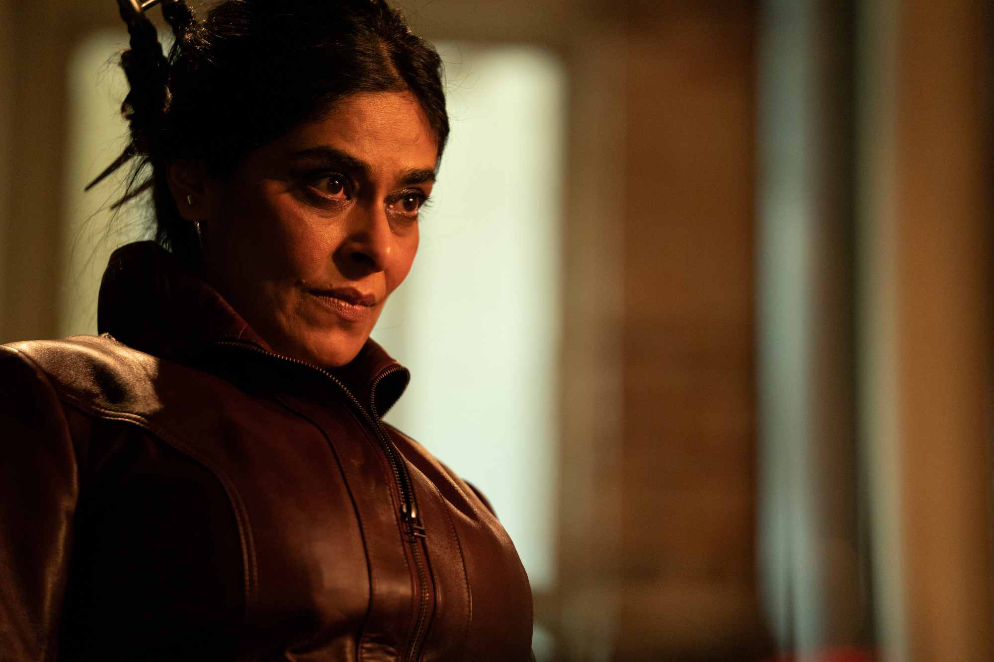 Nimra Bucha as Najma in 'Ms. Marvel,' which has an episode 4 release date of June 29. Her hair is pulled back and she's standing in a dimly lit room.