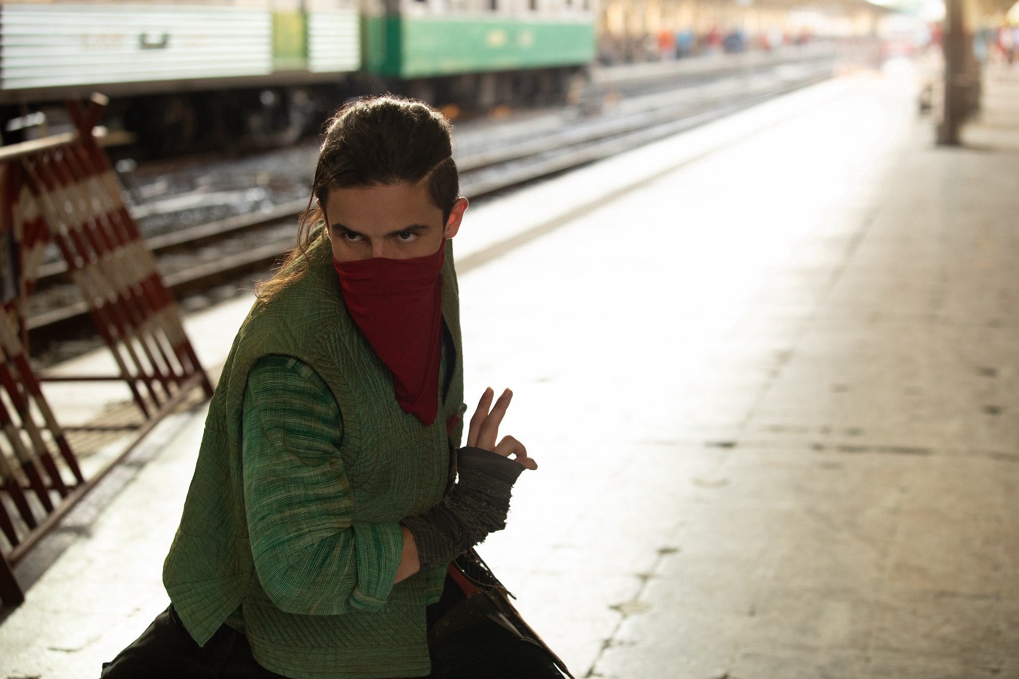 Aramis Knight, in character as Red Dagger in 'Ms. Marvel' Episode 4, wears a green vest over a green long-sleeved shirt and a red scarf around the lower half of his face.