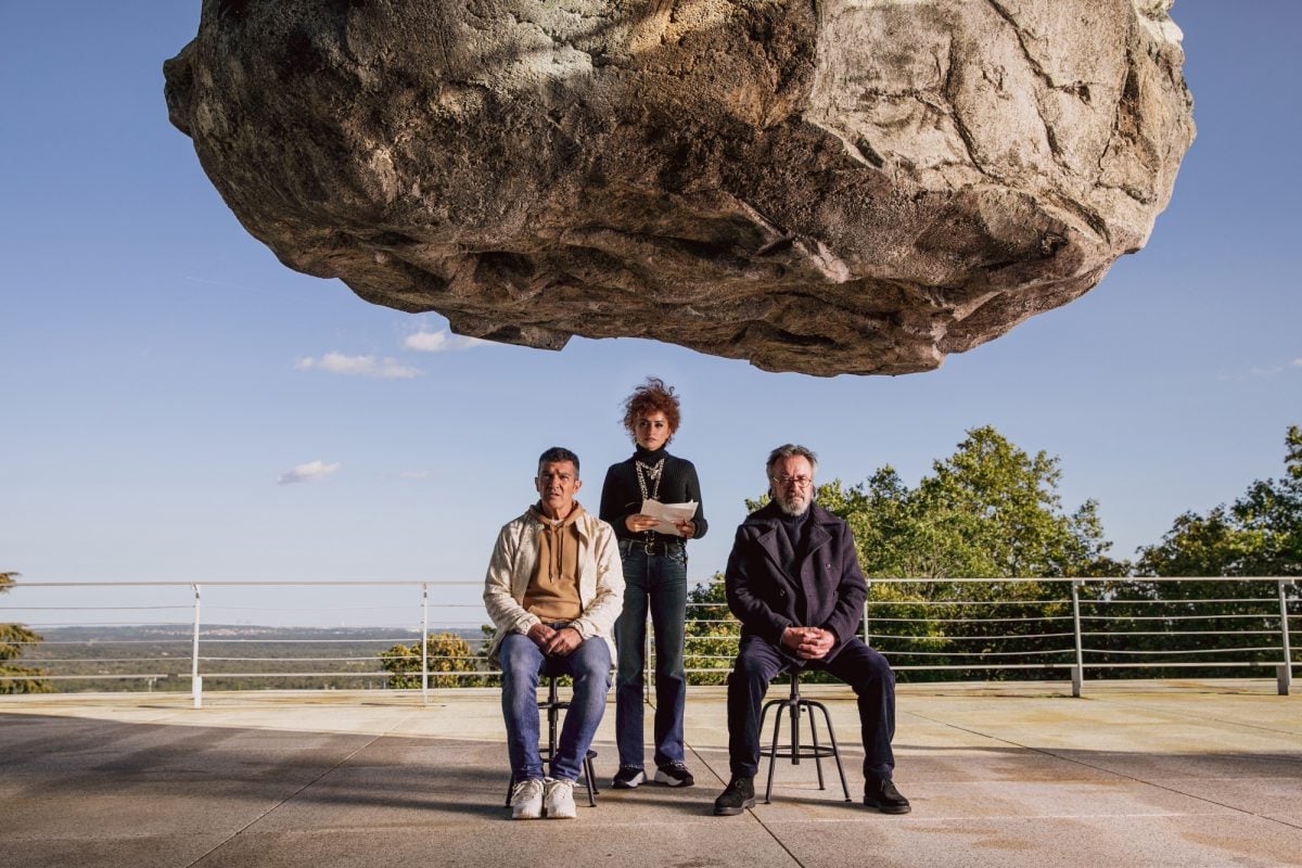 'Official Competition' Antonio Banderas as Félix Rivero, Penélope Cruz as Lola Cuevas, and Oscar Martínez as Iván Torres. Banderas and Martínez are sitting in chairs under a suspended heavy rock, while Cruz stands behind them.