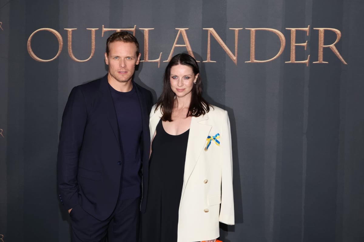 Outlander stars Sam Heughan and Caitriona Balfe attend the season 6 premiere, posing in front of the Outlander logo