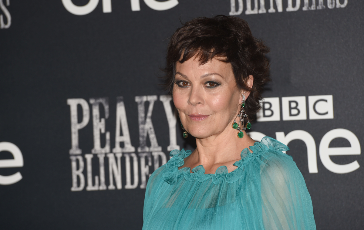 Helen McCrory portrays Polly in Peaky Blinders. The actor wears a sheer blue tops and dangly green earrings.