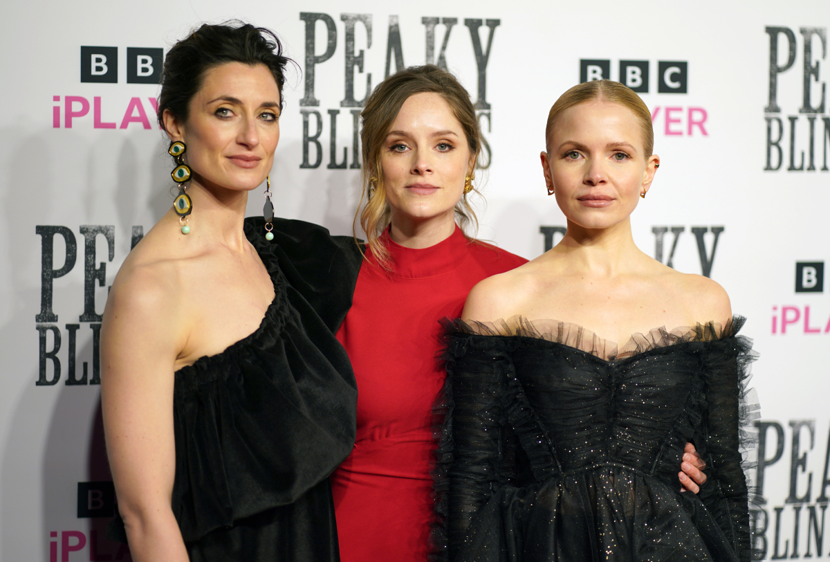Natasha O'Keeffe, Sophie Rundle and Kate Phillips attending the premiere for Peaky Blinders Season 6. O'Keefe and Phillips wear black dresses while Rundle wears red. 