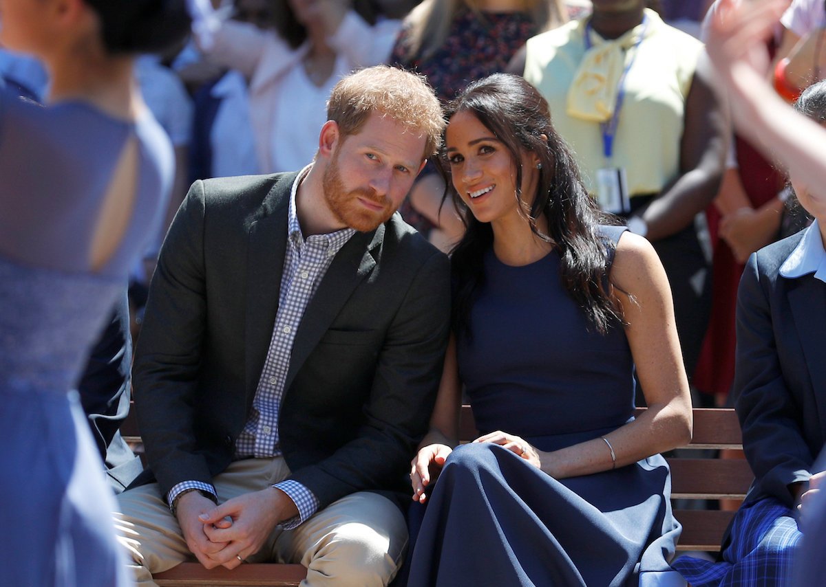 Prince Harry and Meghan Markle, who a royal author says could be the reason for more photos of Prince George, Princess Charlotte, and Prince Louis, smile and look on