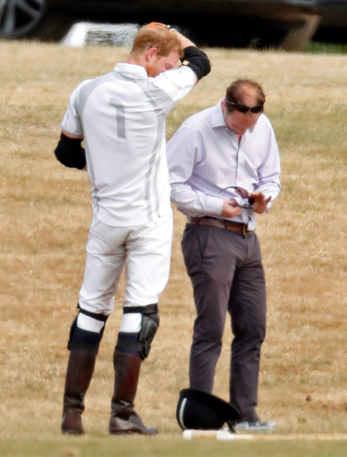 Prince Harry standing by polo manager Andrew Tucker who is cleaning the duke's sunglasses