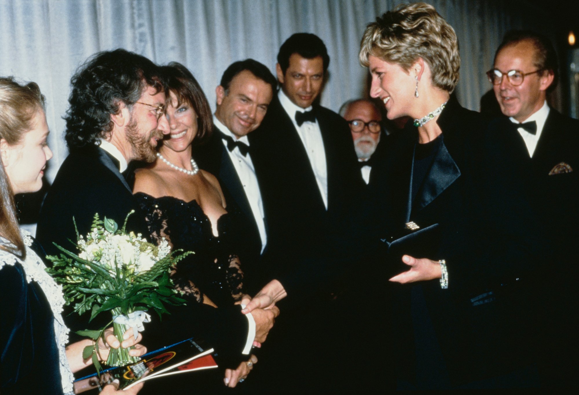 Princess Diana, Ariana Richards, director Spielberg and his wife Kate Capshaw, and stars Sam Neill, Jeff Goldblum and Richard Attenborough at 'Jurassic Park' premiere smiling in formal attire and shaking hands, while the film cast and crew shake hands with Diana.