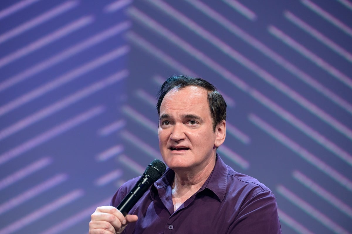 Quentin Tarantino holding a microphone while wearing a purple shirt.