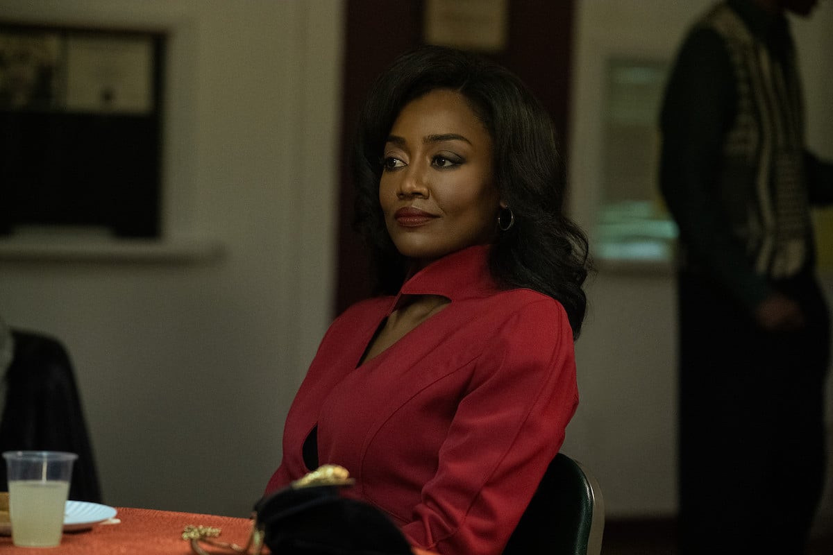 Patina Miller appears as Raquel "Raq" Thomas in a scene from 'Power Book III: Raising Kanan' on Starz. She sits down at a table wearing a red outfit with a smirk on her face.
