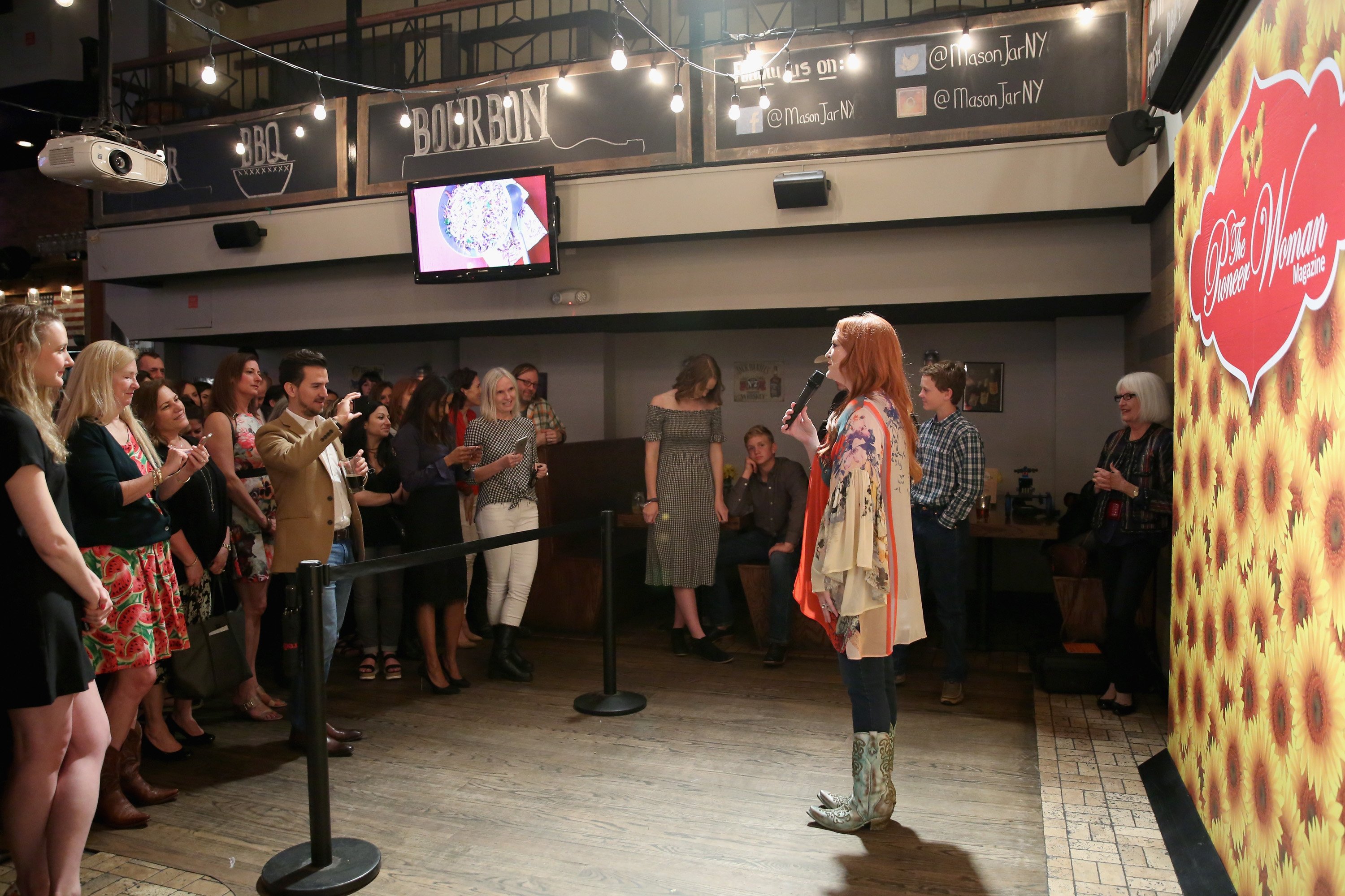 Celebrity chef Ree Drummond wears cowboy boots and a floral top as she speaks to an audience.