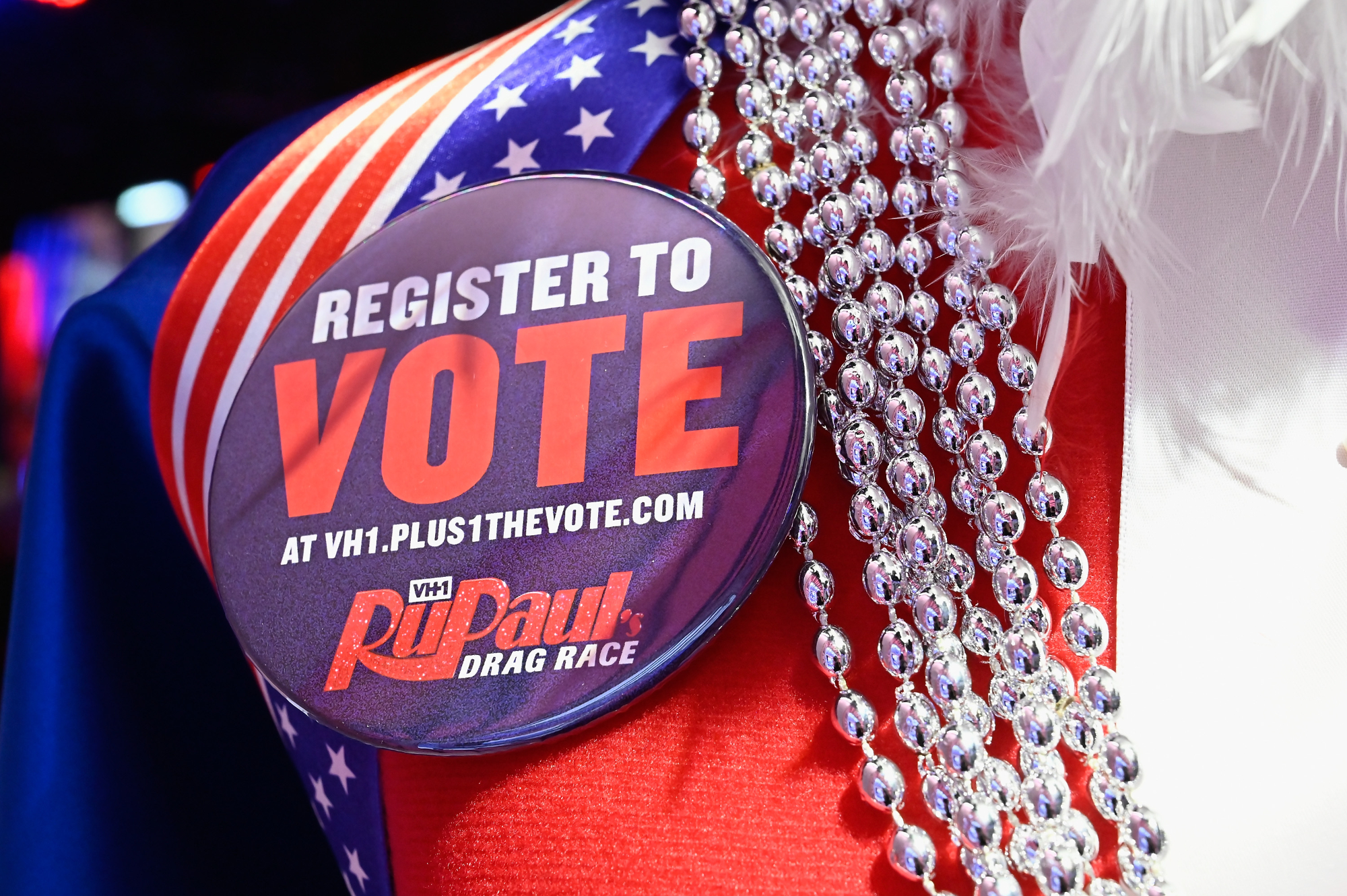'RuPaul's Drag Race' register to vote pin, whose cast is speaking up about Roe v. Wade. Next to the pin is a beaded necklace.