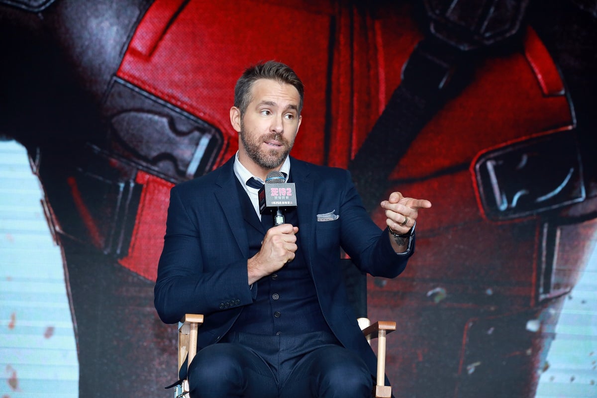 Ryan Reynolds sitting down and holding a microphone.