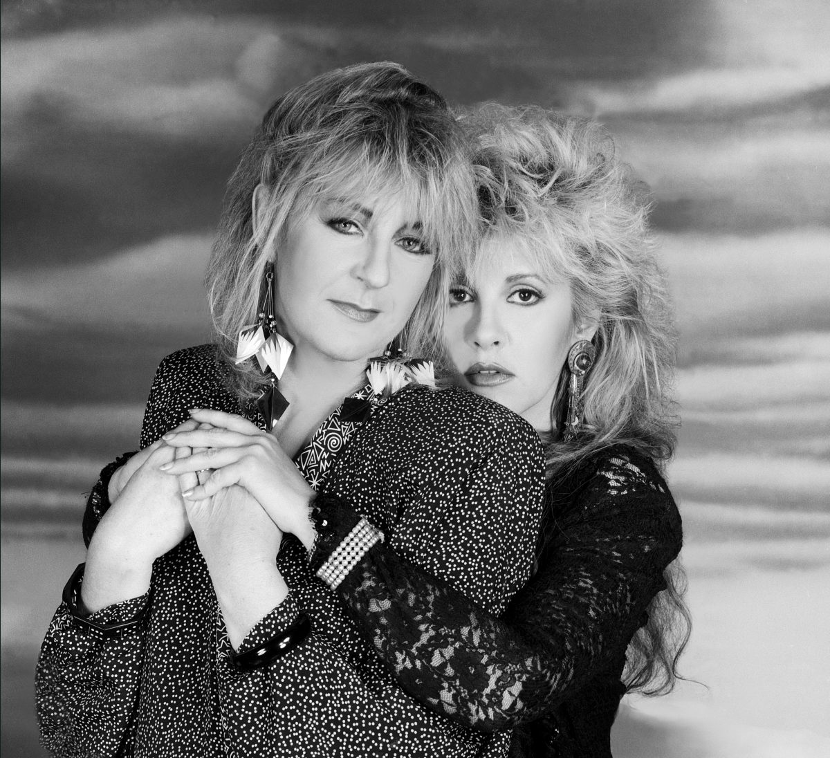 A black and white picture of Stevie Nicks wrapping her arms around Christine McVie.