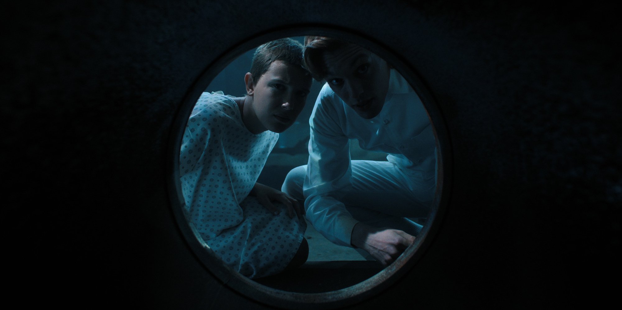 'Stranger Things 4' characters Eleven and Henry/001 peer into a tunnel in a production still.