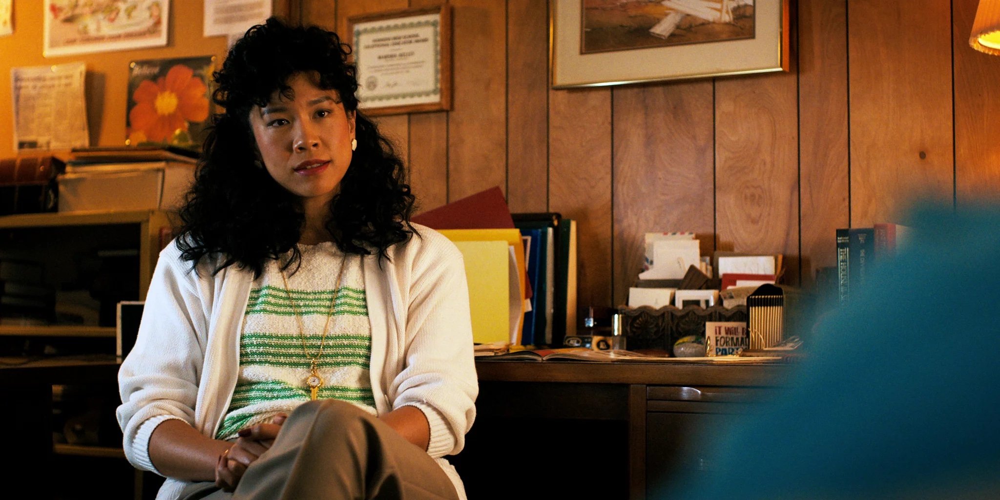 'Stranger Things 4' star Regina Ting Chen as Ms. Kelly wearing a green and white stropped shirt while wearing a clock pendant.