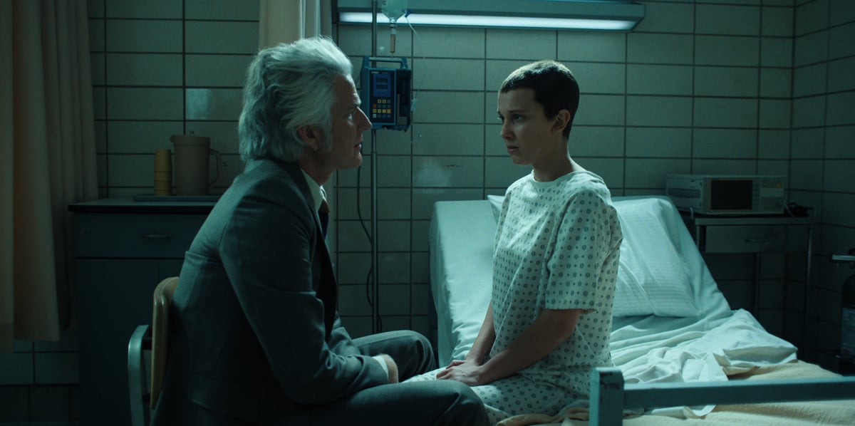 Matthew Modine as Dr. Martin Brenner and Millie Bobby Brown as Eleven in Stranger Things Season 4. Dr. Brenner sits with Eleven at Hawkins Lab.