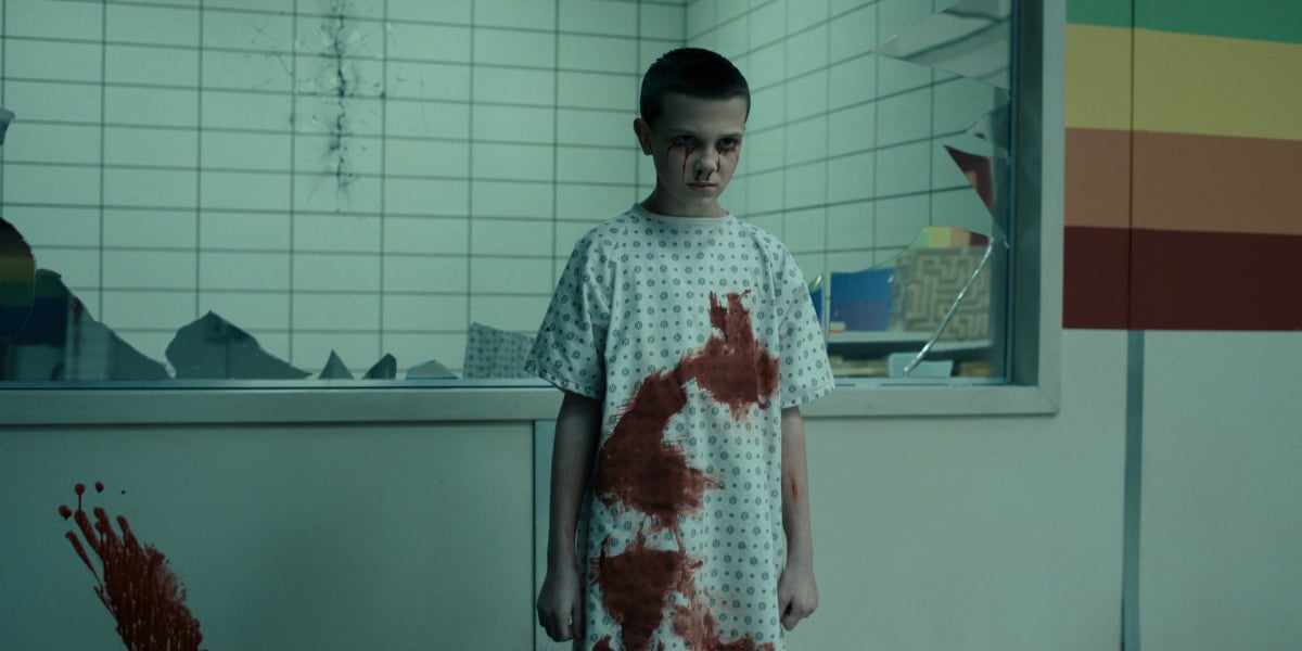 Eleven opening the Upside Down in Stranger Things. Nine-year-old Eleven has blood on her hospital gown and streaked under her eyes.