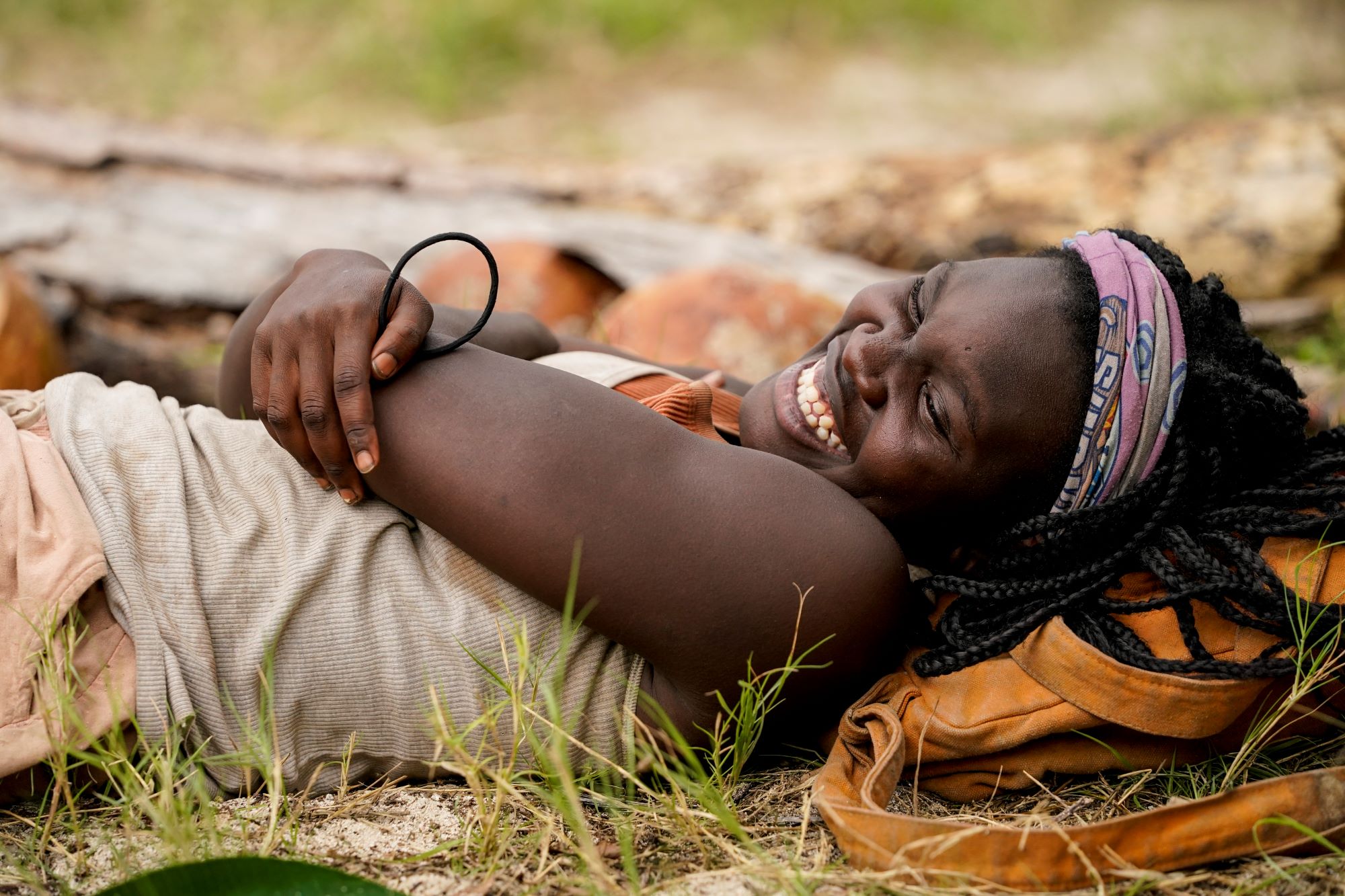 Maryanne Oketch, who won 'Survivor' Season 42 ahead of season 43, which isn't new tonight, wears a gray tank top, tan shorts, and a purple buff on her head while laying on the ground.