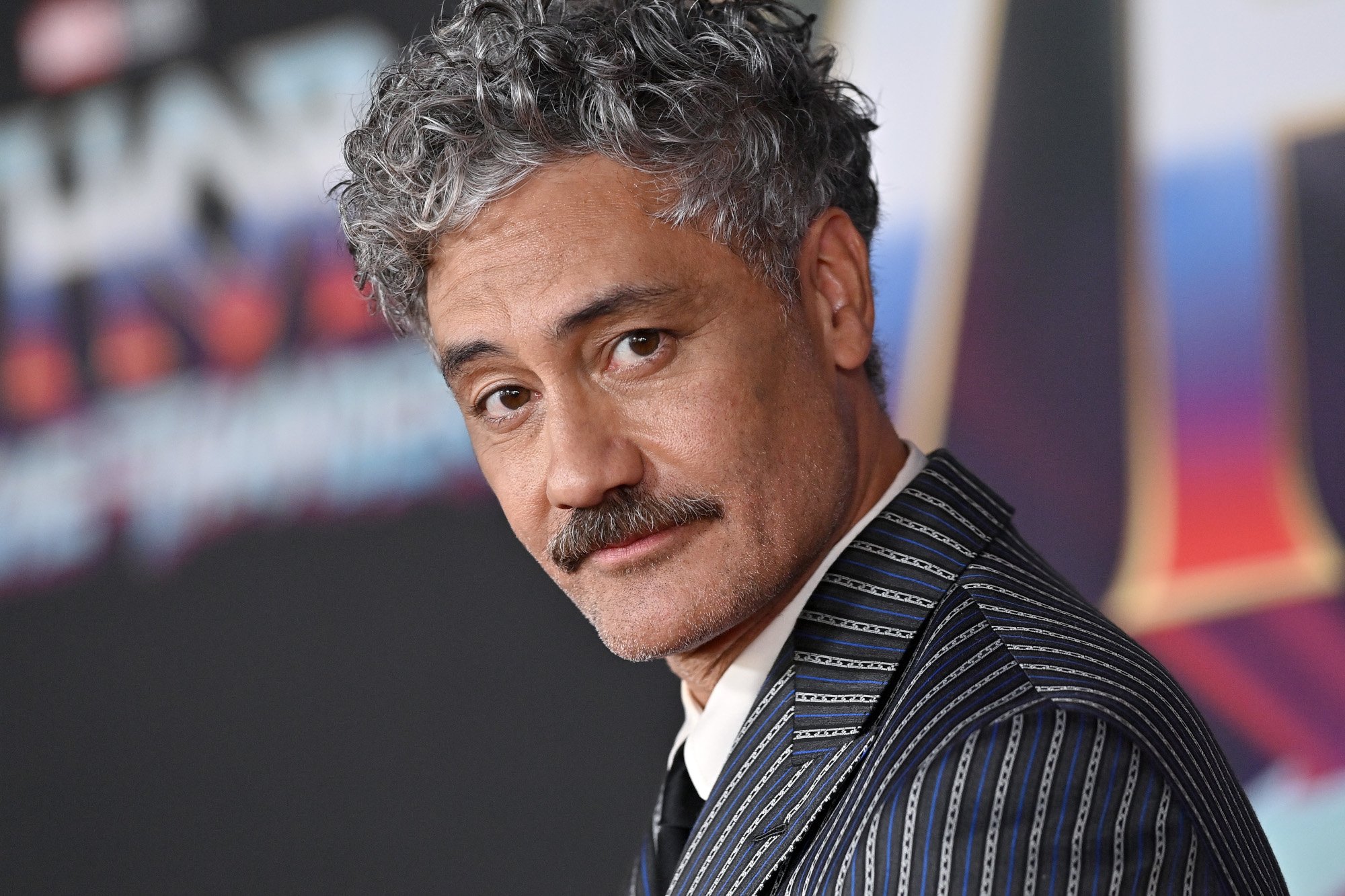 Taika Waititi, who will helm an upcoming 'Star Wars' movie. He's on the red carpet for 'Thor: Love and Thunder,' and he's wearing a black suit with white stripes.