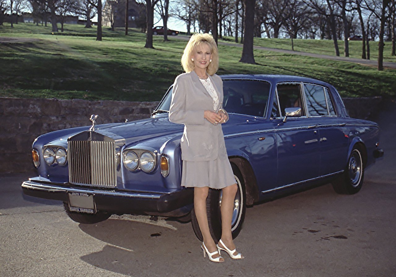 Tammy Wynette, whose net worth was less than $1 million by her death, wearing a gray outfit and posing in front of a blue Rolls-Royce car