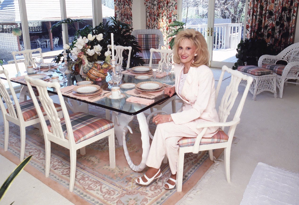 Tammy Wynette, who's net worth was less than $1 million at her time of death, poses in a white suit at a dining table in her home.