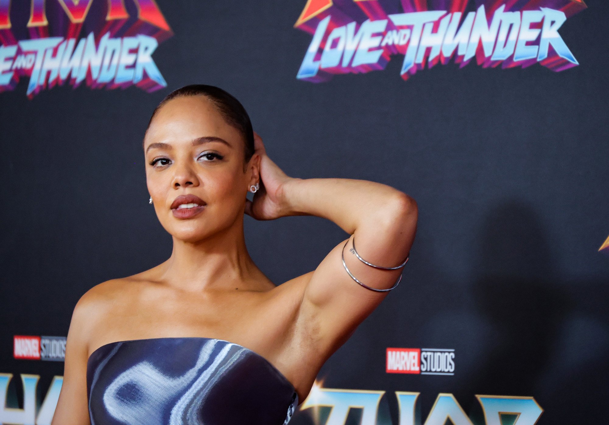 'Thor: Love and Thunder' star Tessa Thompson, who will play Valkyrie as she takes up her title as King of Asgard. She's wearing a dark, metallic dress and holding her hand up to her head.