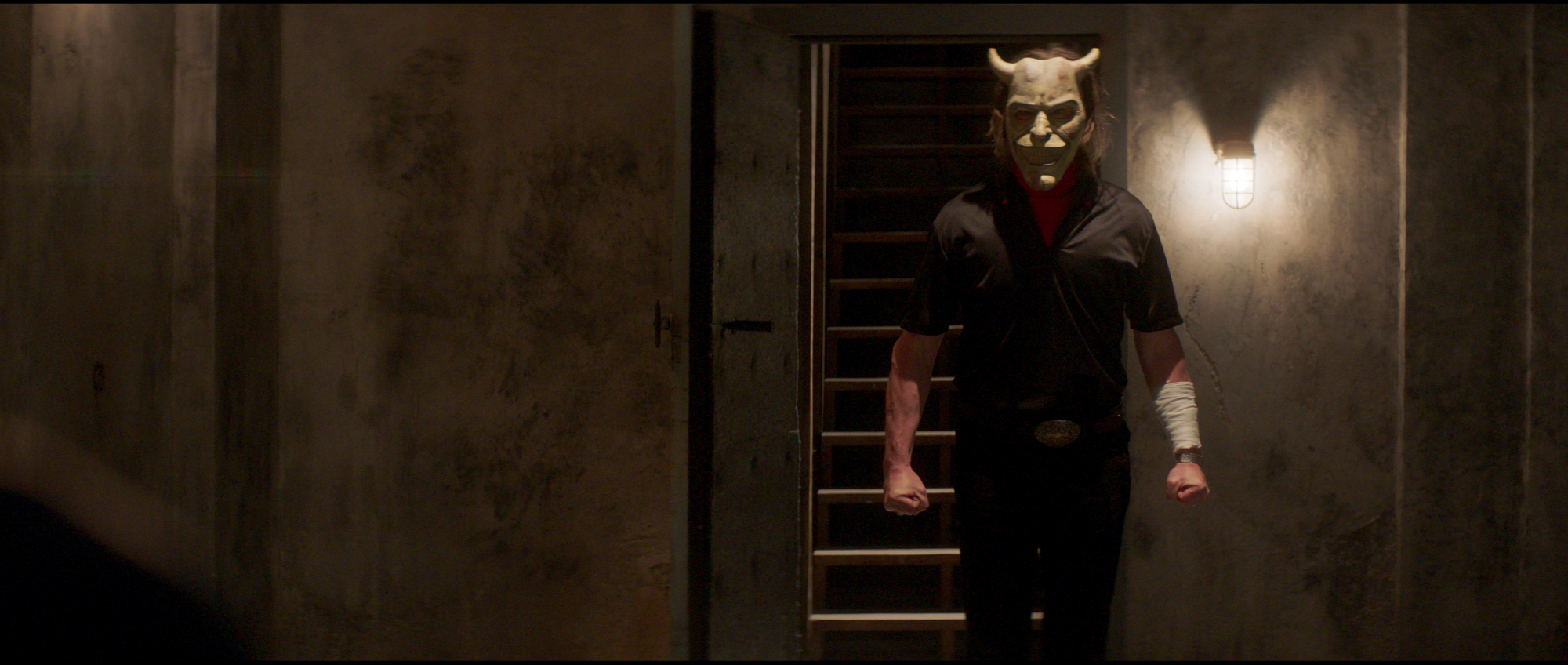 'The Black Phone' Ethan Hawke as The Grabber wearing a smiling demon mask and standing in a stairway