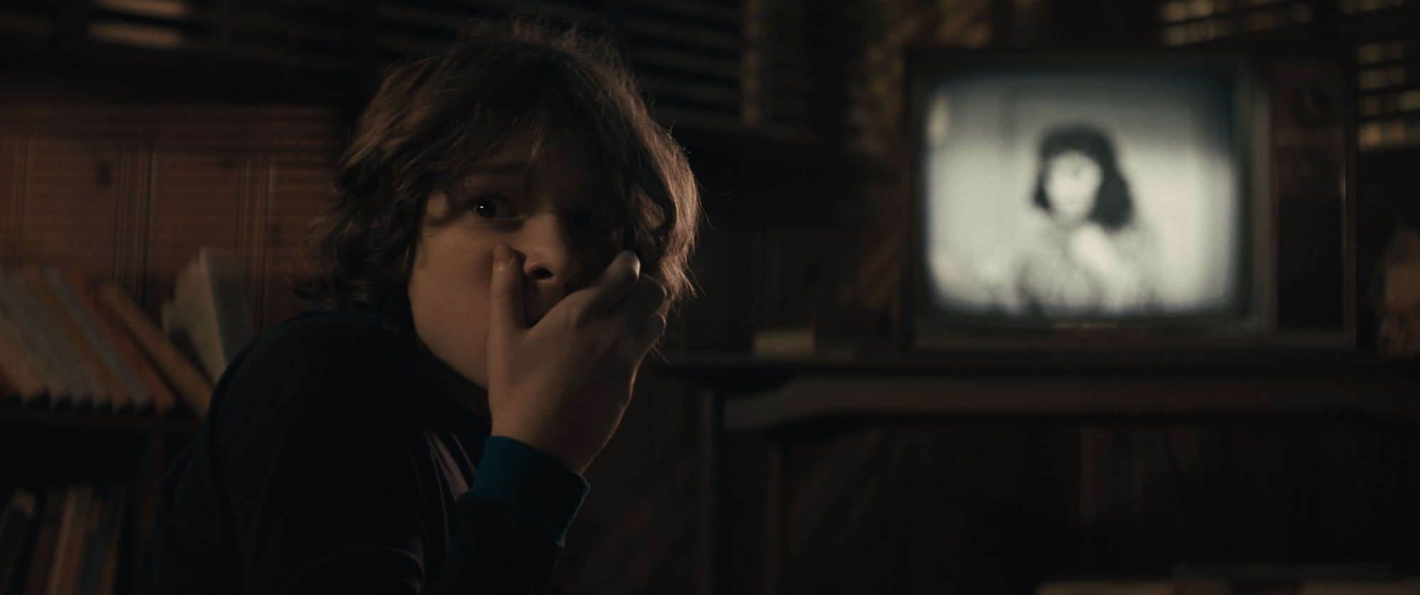 'The Black Phone' Mason Thames as Finney Shaw, which will include new Blumhouse intro with Easter eggs. He's holding his hand over his mouth in front of a television screen.