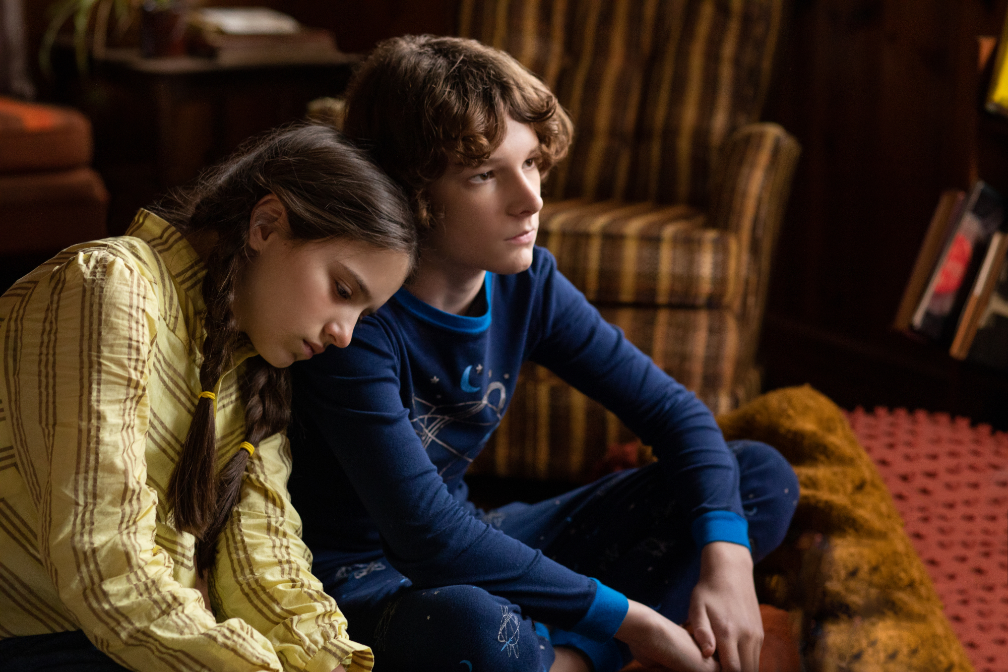 'The Black Phone' scene with Madeleine McGraw as Gwen Shaw and Mason Thames as Finney Shaw with Gwen resting her head on Finney's shoulder with a sofa couch in the background.