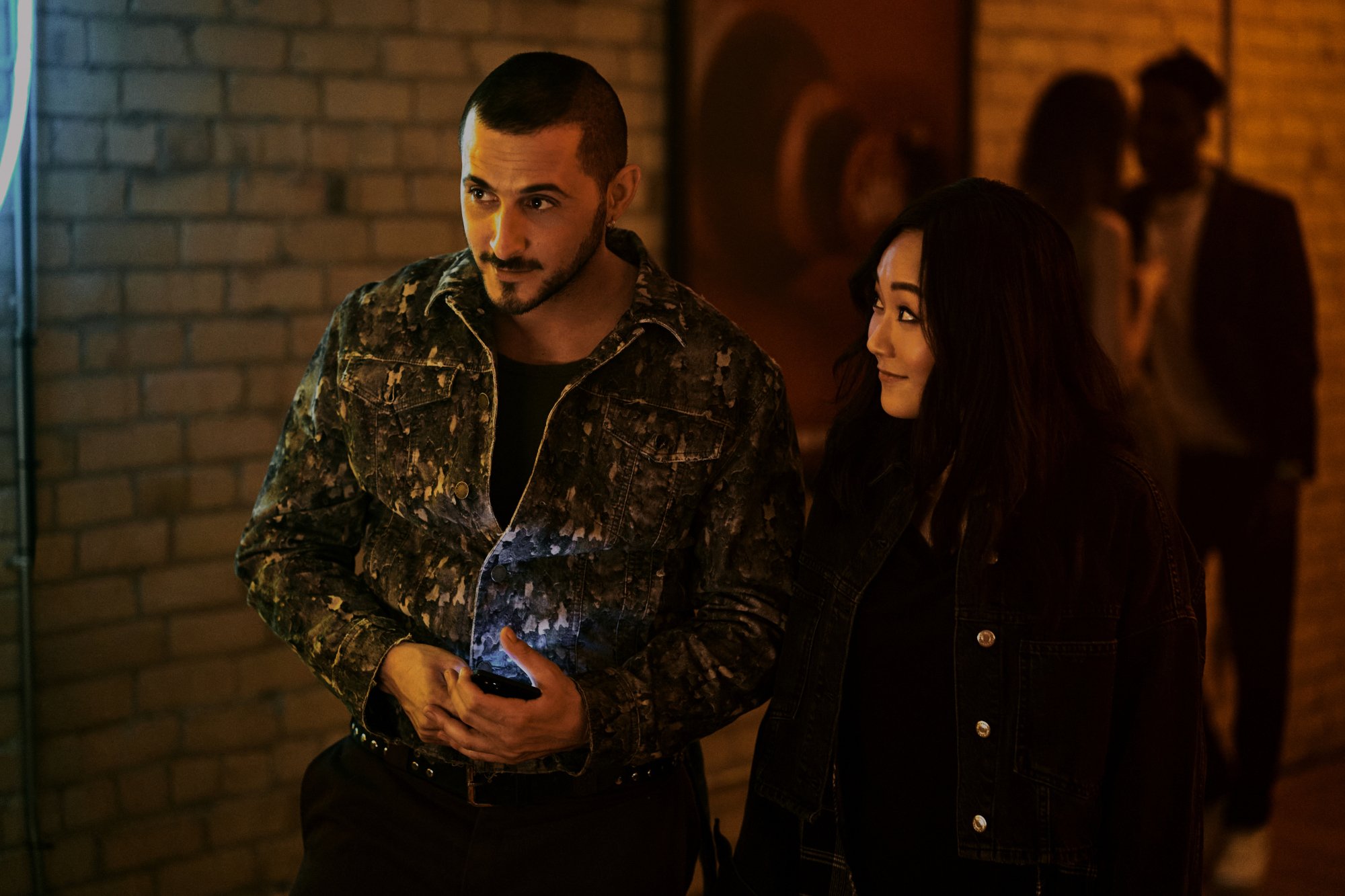 Tomer Capone and Karen Fukuhar in the opening scene of 'The Boys' Season 3. He's holding a jar and looking at something off-screen. She's looking at him and smiling.