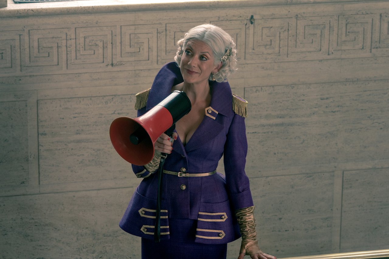 Kate Walsh as The Handler in 'The Umbrella Academy' stands in a purple outfit holding a blowhorn.