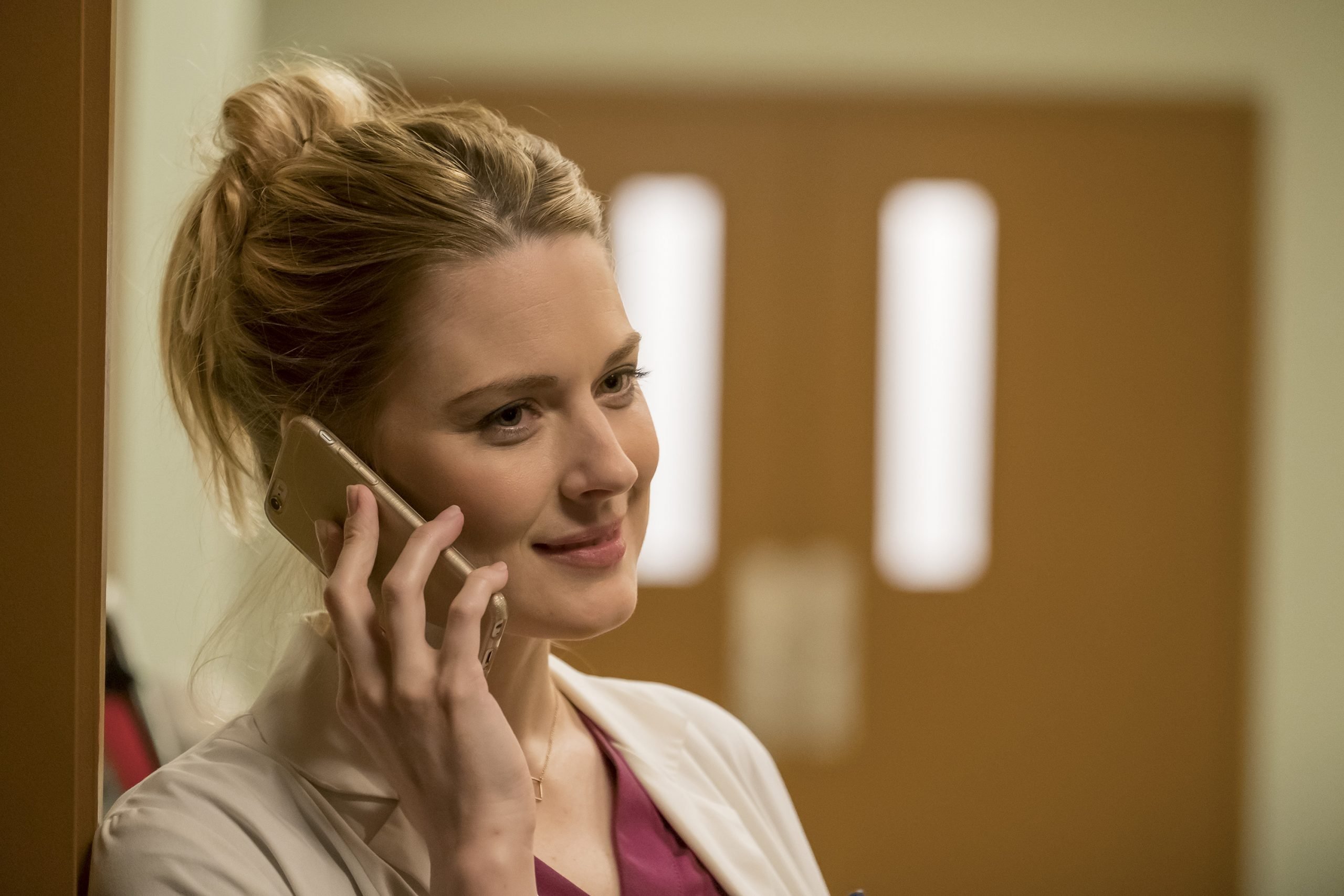 Alexandra Breckenridge, in character as Sophie in 'This Is Us' Season 1, wears a white doctor's coat over dark red scrubs and holds her cell phone to her ear.