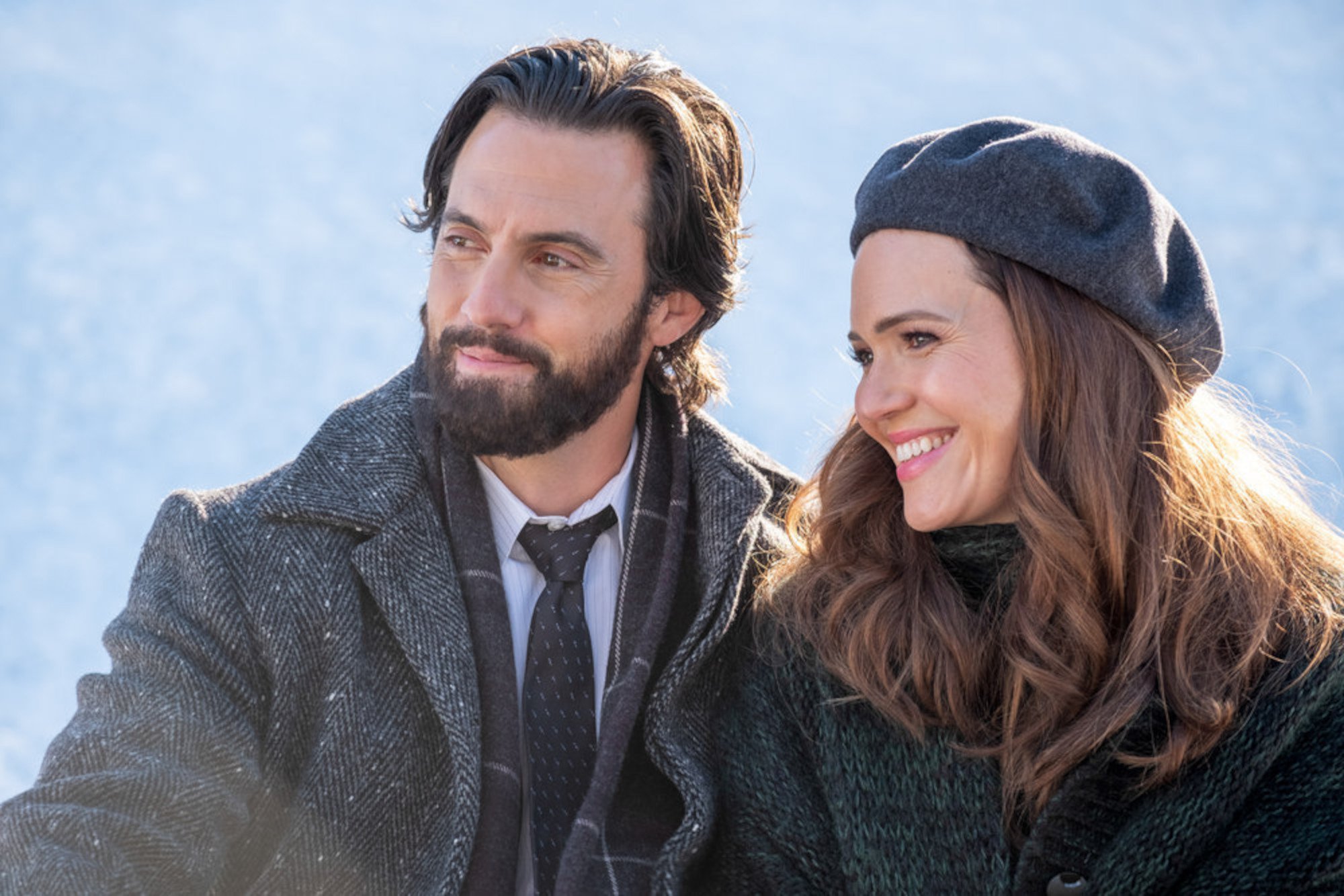 Milo Ventimiglia and Mandy Moore as Jack and Rebecca Pearson in 'This Is Us' Season 6. The two are sitting in the snow, wearing coats. They're smiling and looking at something off-screen.