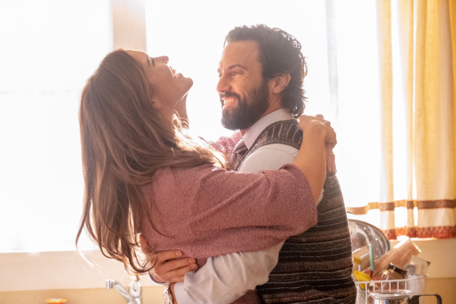 Mandy Moore and Milo Ventimiglia as Rebecca and Jack Pearson in 'This Is Us,' which was originally almost 4 seasons. Jack is holding Rebecca, and she's laughing. They're in front of a window, and sunlight is pouring in.