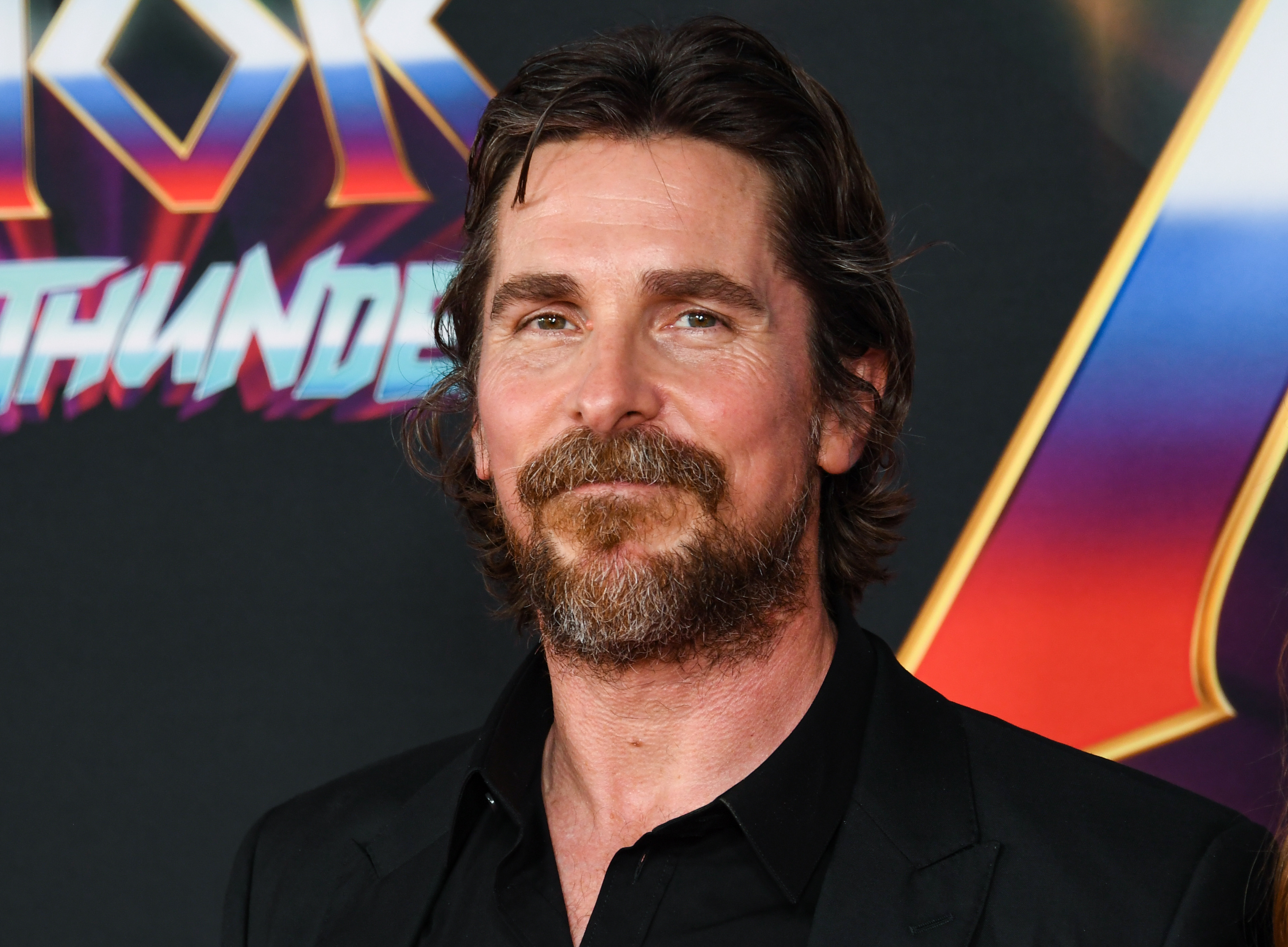Christian Bale, who stars as Gorr the God Butcher in 'Thor: Love and Thunder,' wears a black suit over a black button-up shirt.