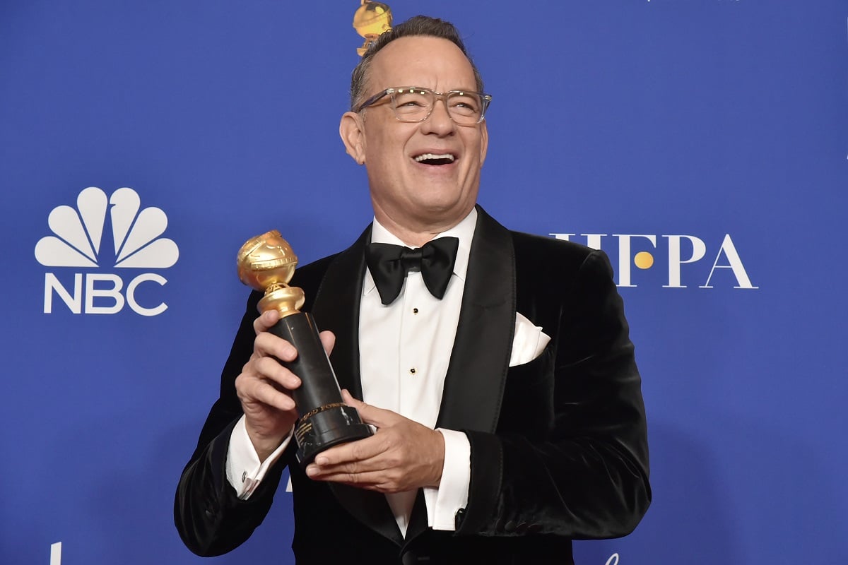 Tom Hanks smiling in a suit while holding a statue.