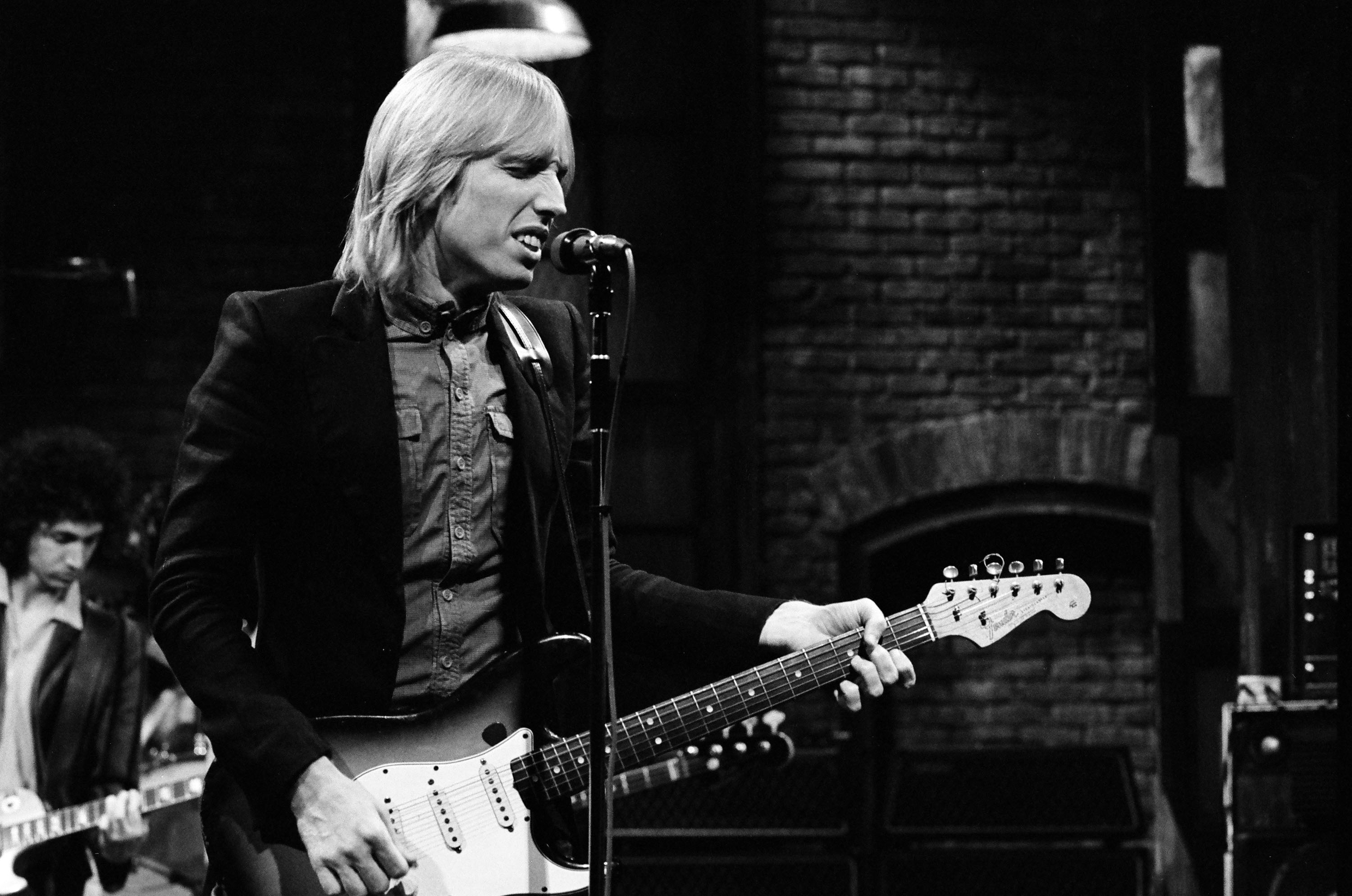 A black and white picture of Tom Petty playing guitar and singing into a microphone on 'SNL.'