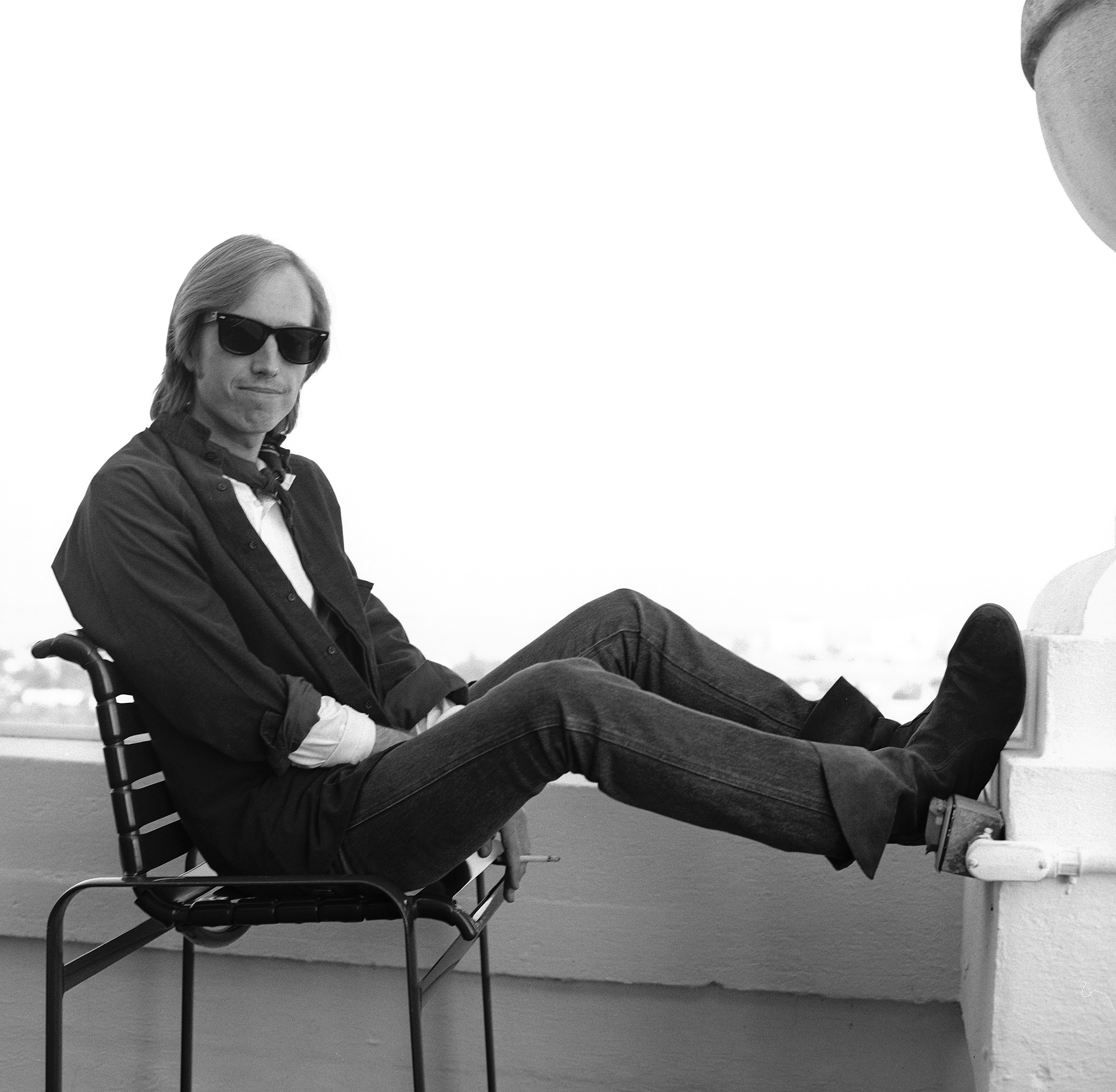 A black and white picture of Tom Petty sitting in a chair and resting his feet on a wall.