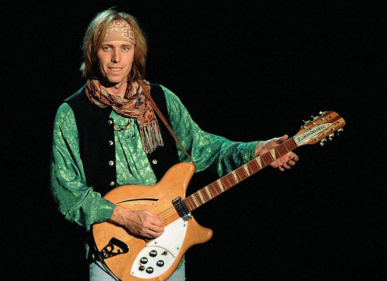 Tom Petty wears a green shirt and strums a guitar.