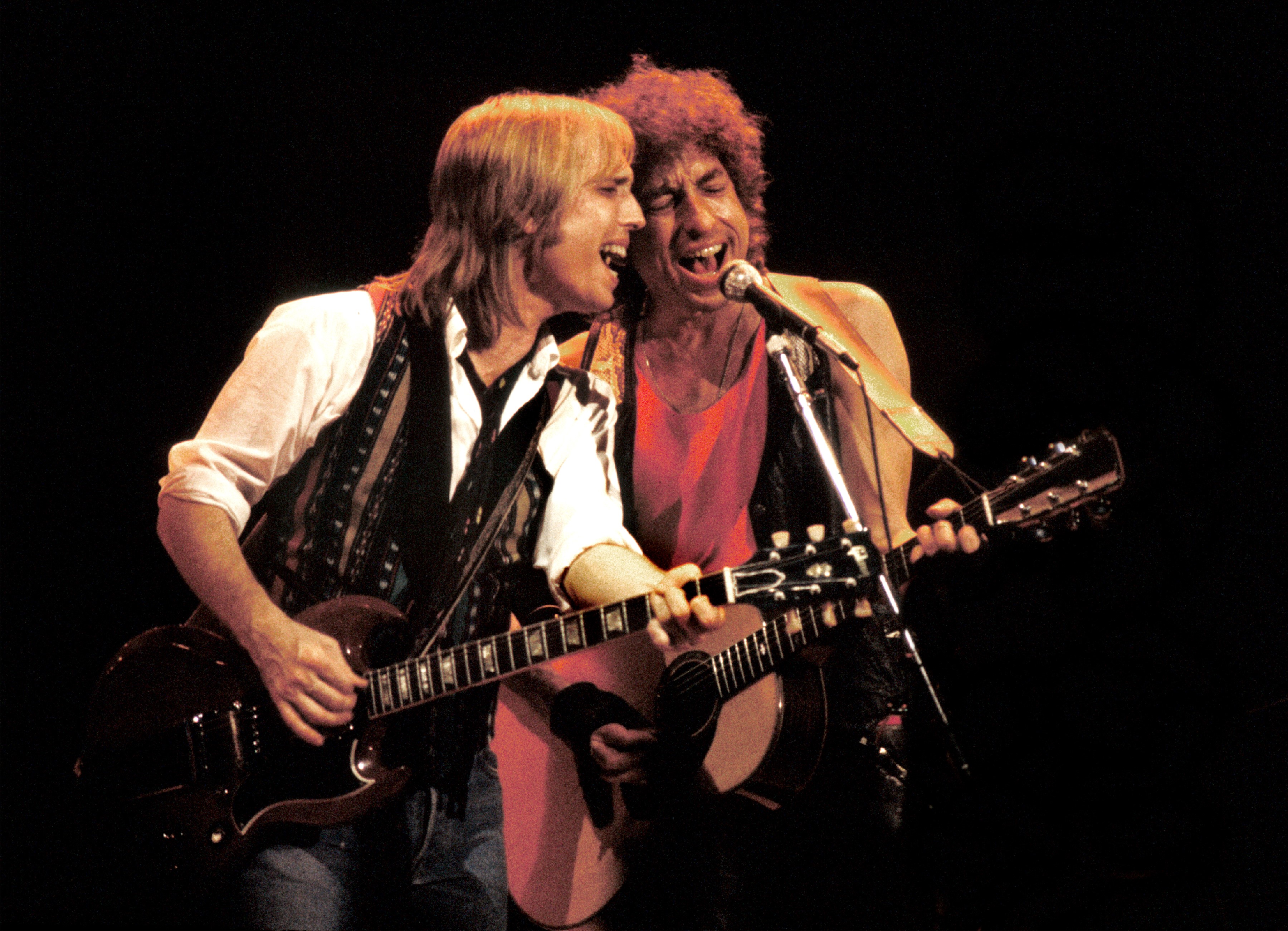 Tom Petty and Bob Dylan play guitar together and sing into the same microphone.