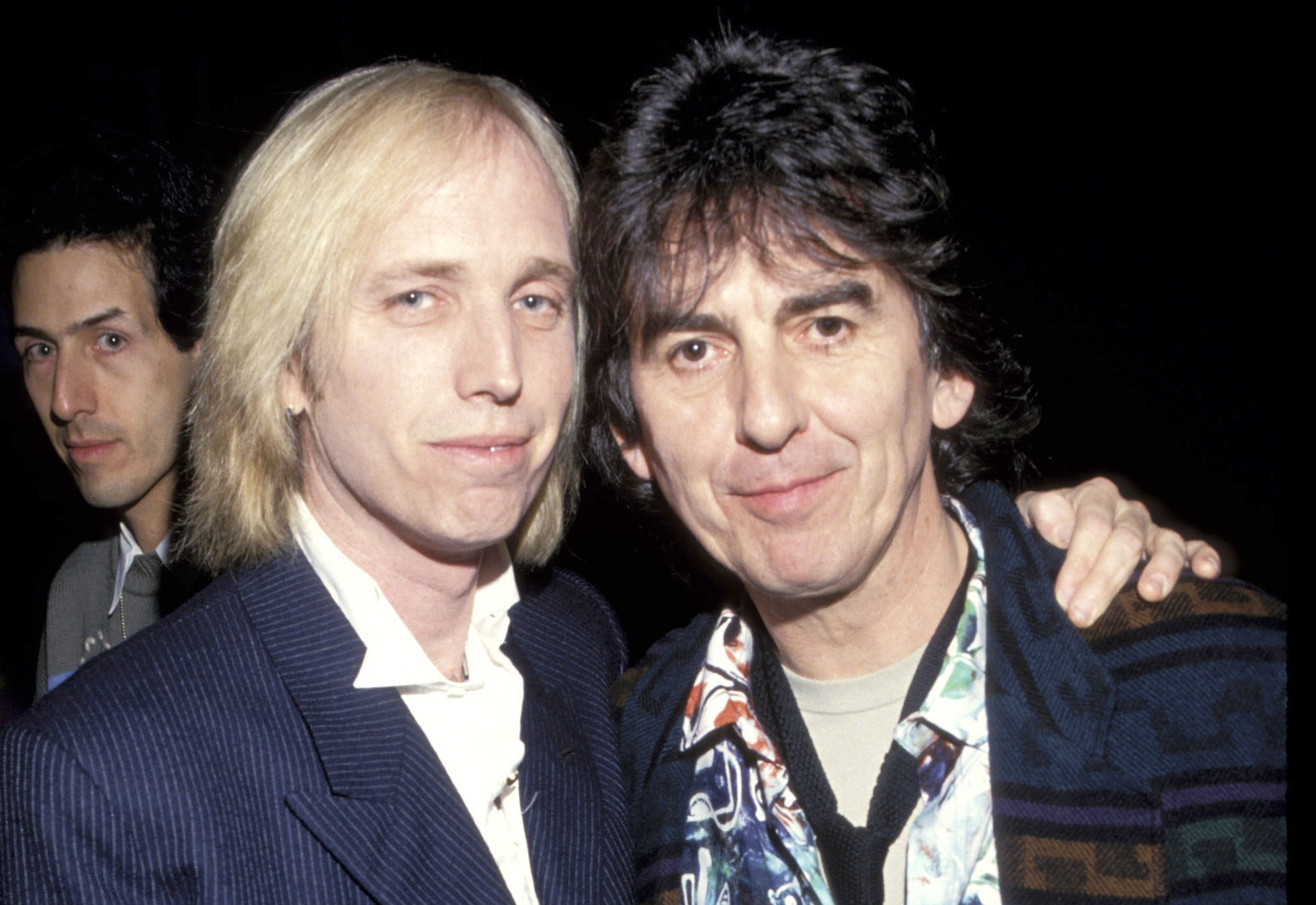Tom Petty stands with his hand on George Harrison's shoulder.