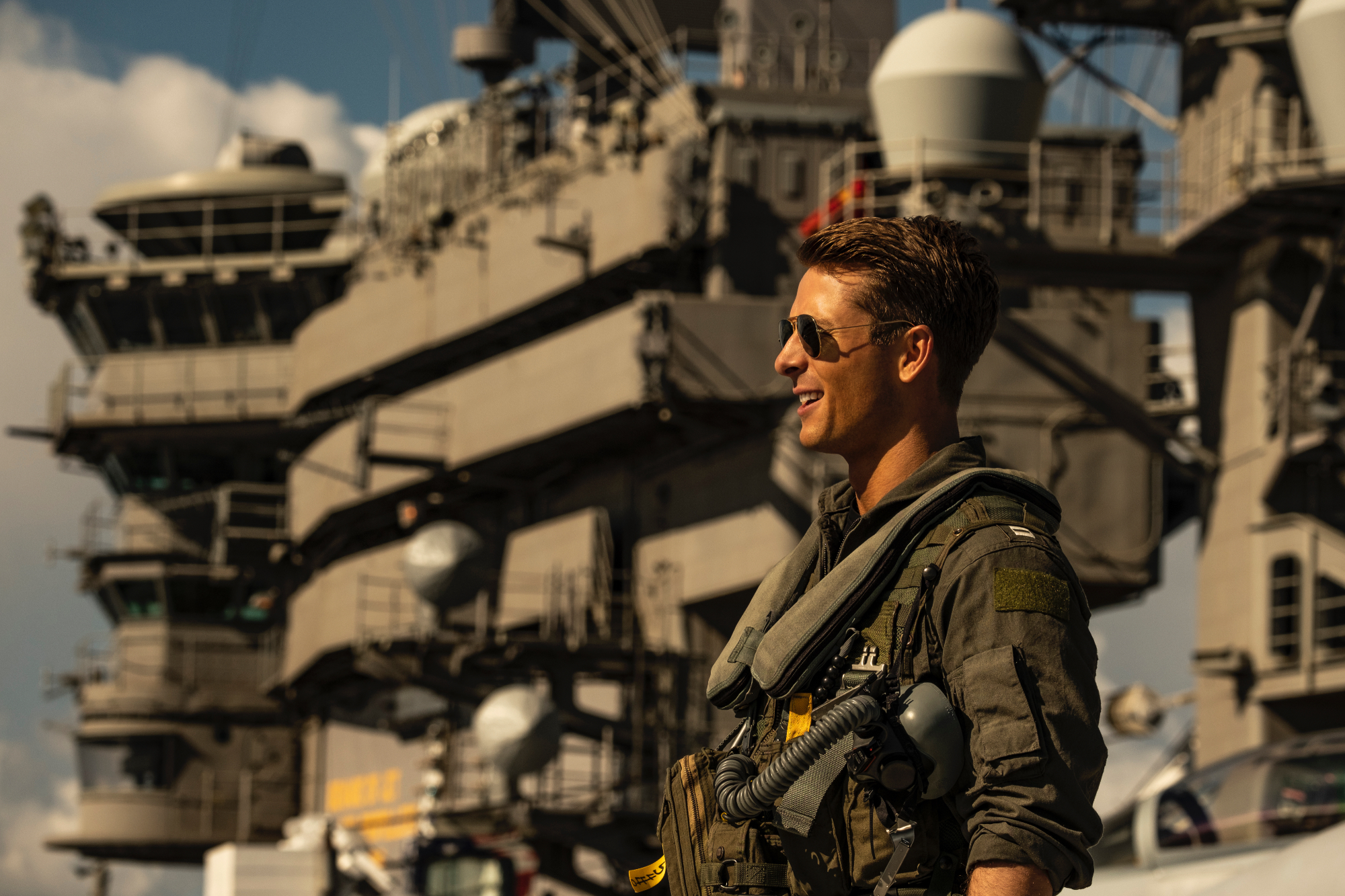 'Top Gun: Maverick' Glen Powell as Hangman, who starred in the iconic beach football scene. He's smiling wearing sunglasses and his pilot uniform.