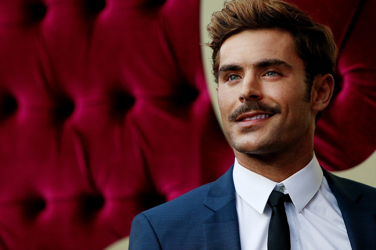 Zac Efron smiling while wearing a suit.