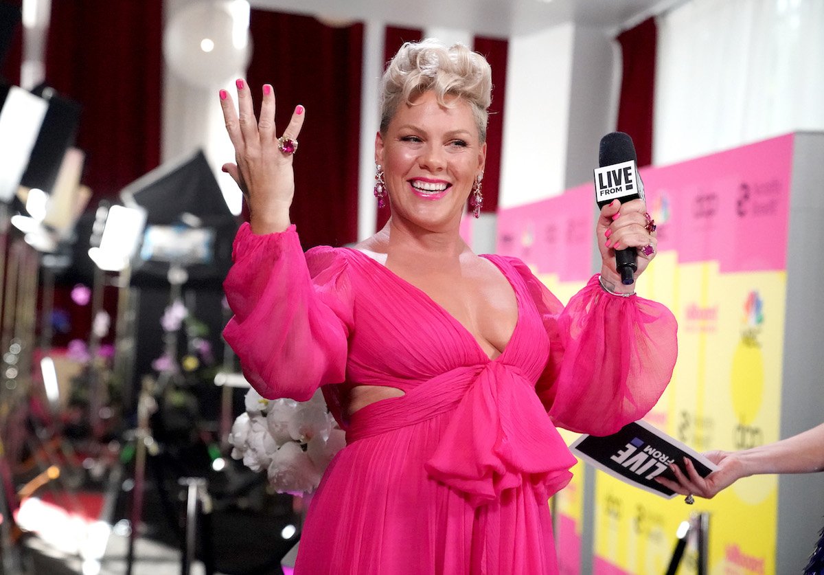 Pink in a pink outfit holding a microphone and holding up her hands smiling