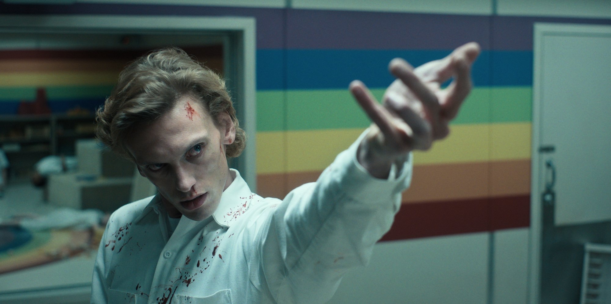 'Stranger Things 4' Jamie Campbell Bower raises his arm in a blood splattered orderly uniform in a production still.