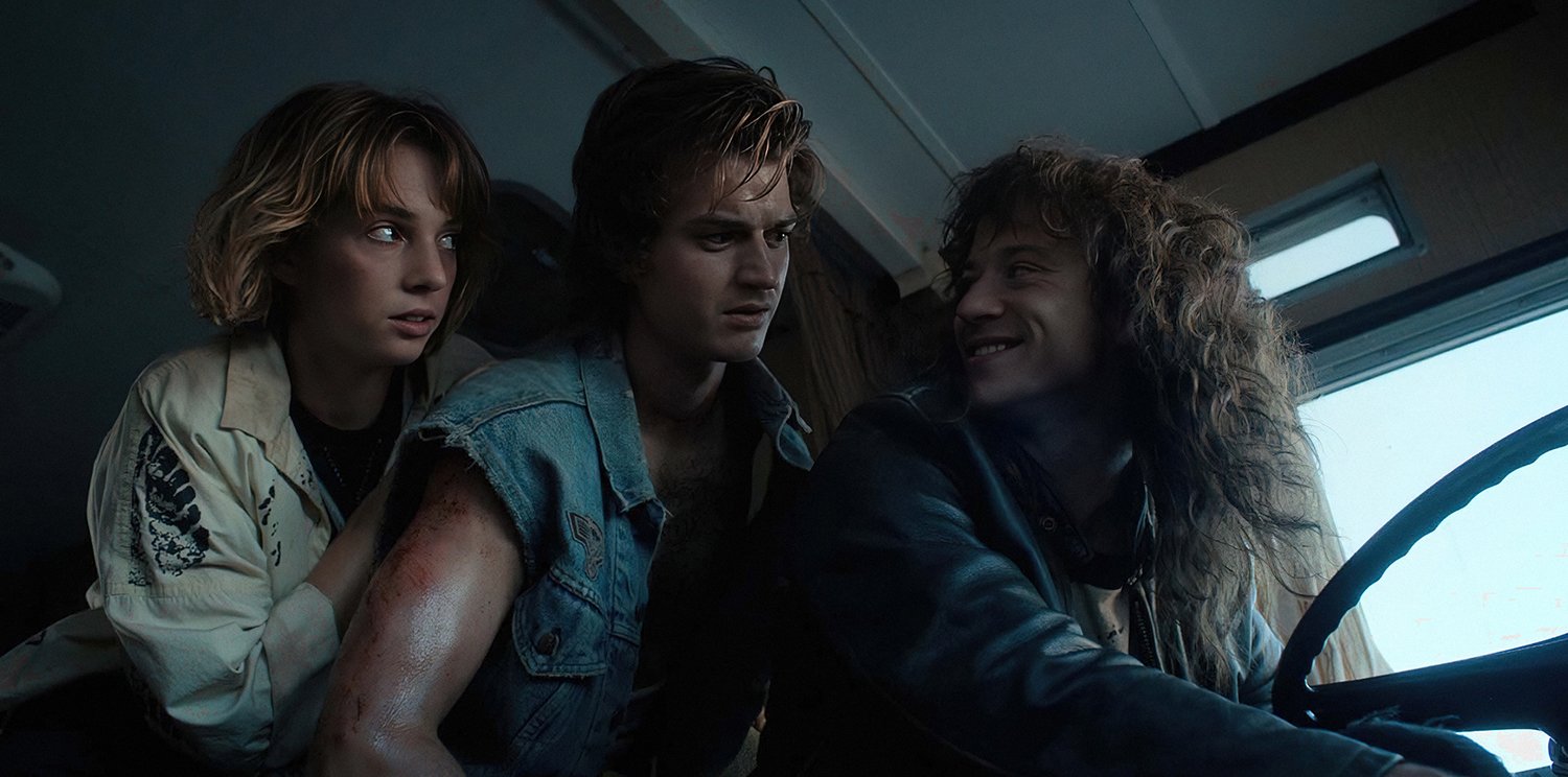 Maya Hawke as Robin and Joe Keery as Steve looking over at Joseph Quinn as Eddie Munson in Stranger Things 4