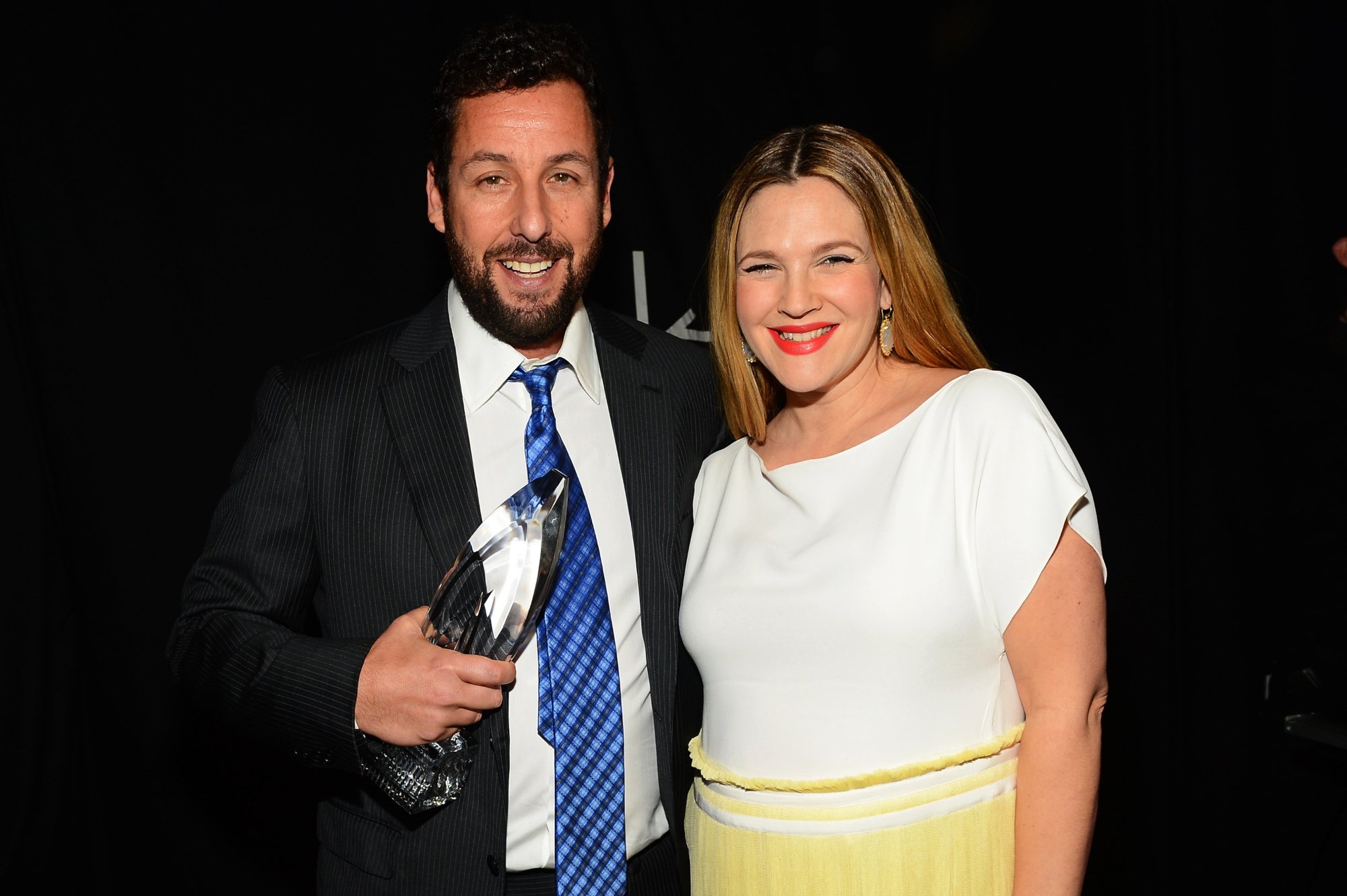 Adam Sandler and Drew Barrymore, who co-starred in 'The Wedding Singer' smiling with Sandler holding a People's Choice Award
