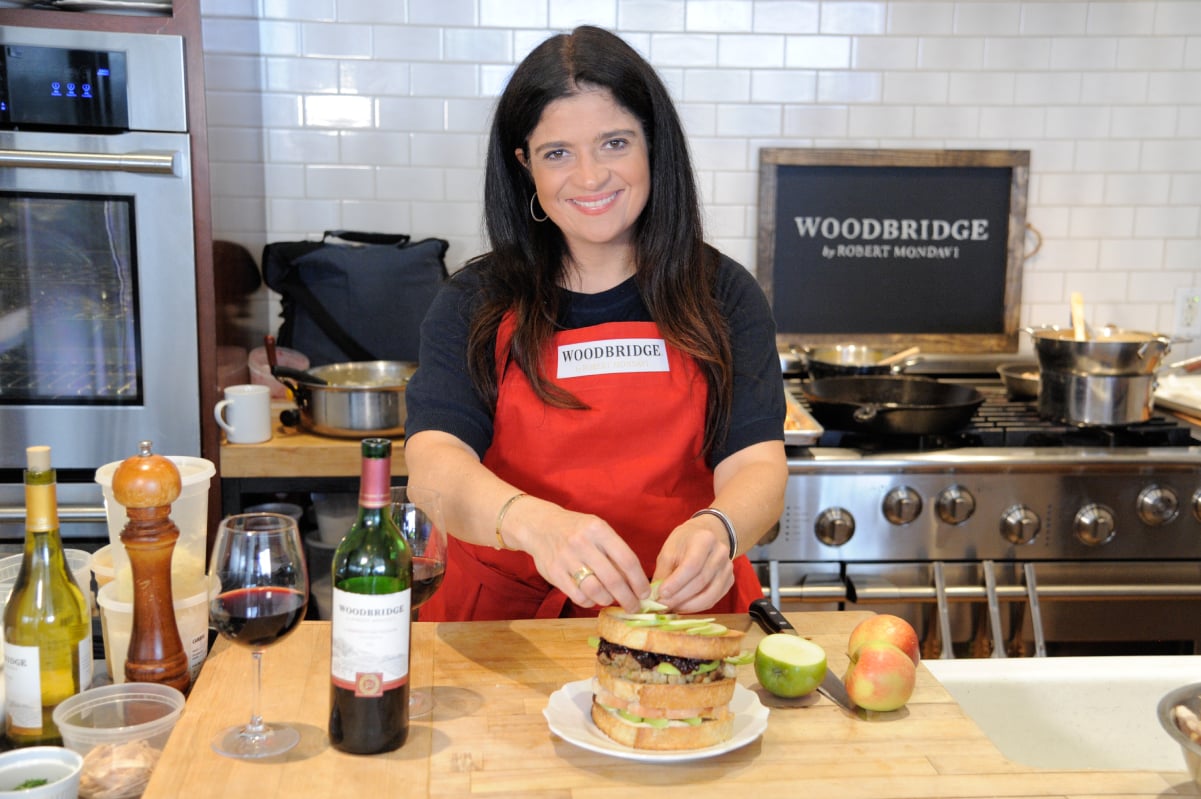 Food Network chef Alex Guarnaschelli wears a red apron and dark blue blouse in this photograph.