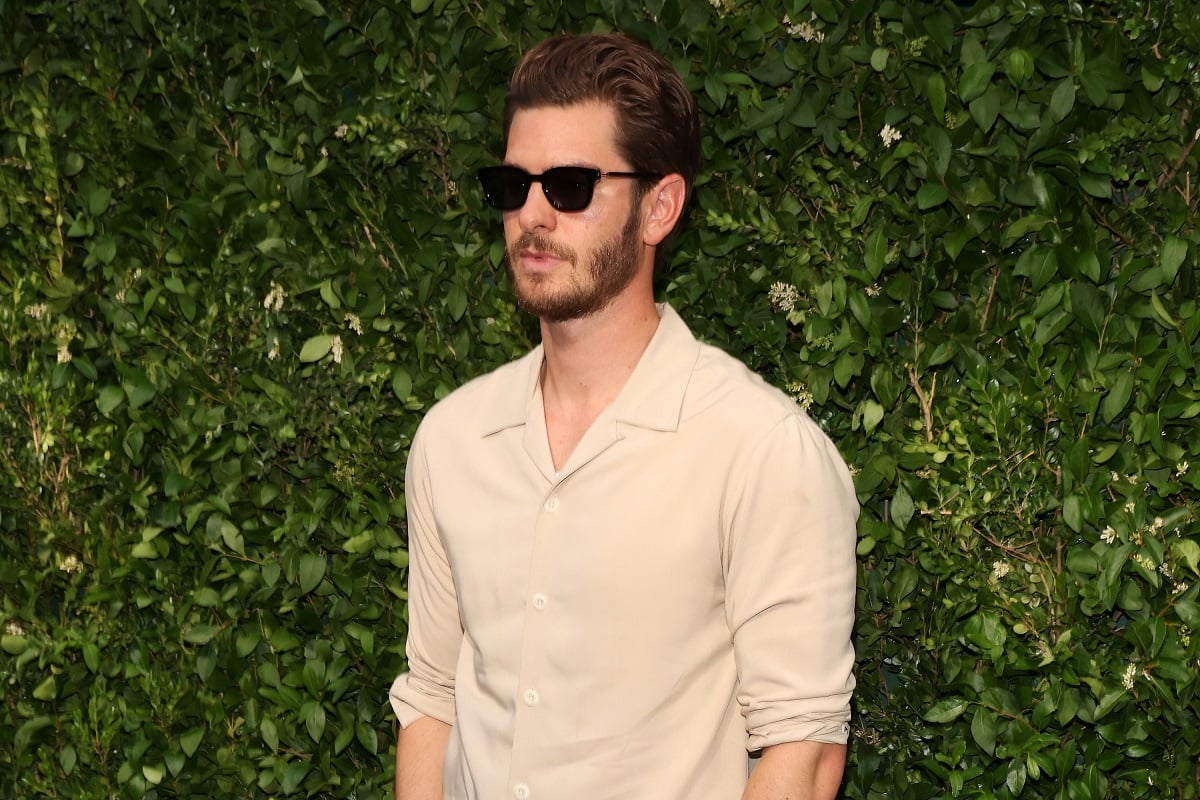 Andrew Garfield standing in front of a bush.