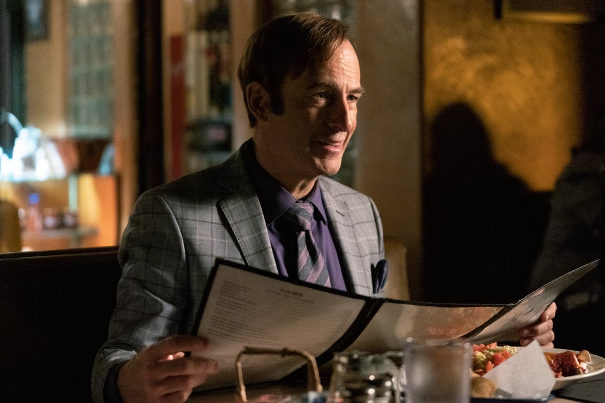 A familiar character may return in the Better Call Saul episode Fun and Games. Saul Goodman sits at a restaurant table holding a menu.