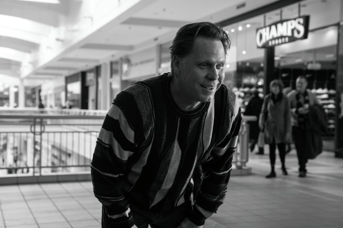 Don Harvey as Jeff the Cabbie in Better Call Saul Season 5. Jeff crouches forward at the mall wearing a striped sweater. 