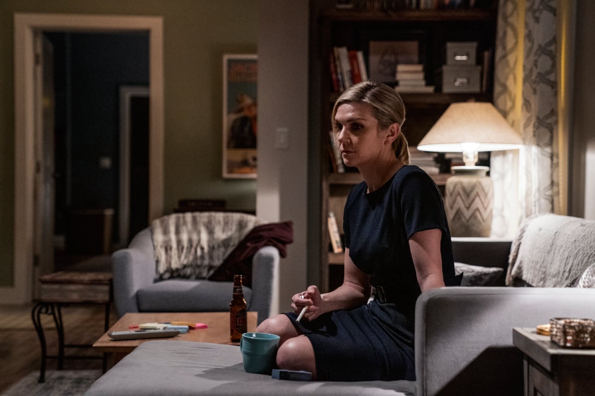 Rhea Seehorn as Kim Wexler in Better Call Saul Season 6. Kim sits on the couch with a cigarette between her fingers.